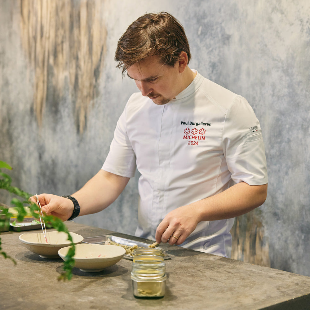 Michelin chef works in the kitchen wearing a white, short-sleeve men's chef coat with a mandarin collar and a front pocket.
