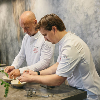 A Michelin rated culinary team repairs dishes in white chef coats with breathable mesh panels, and pin slots