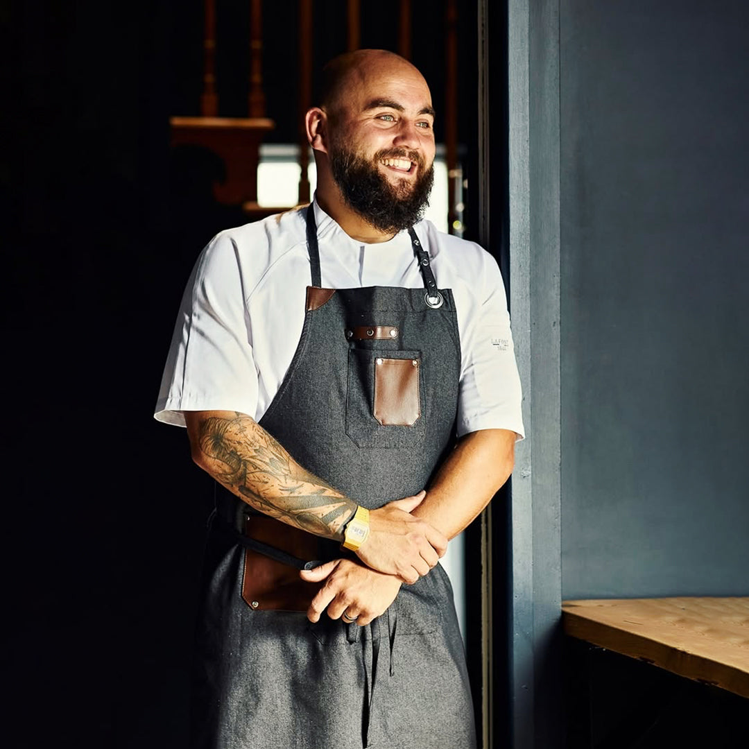 Man standing in a best selling bib apron made of denim with unique features 